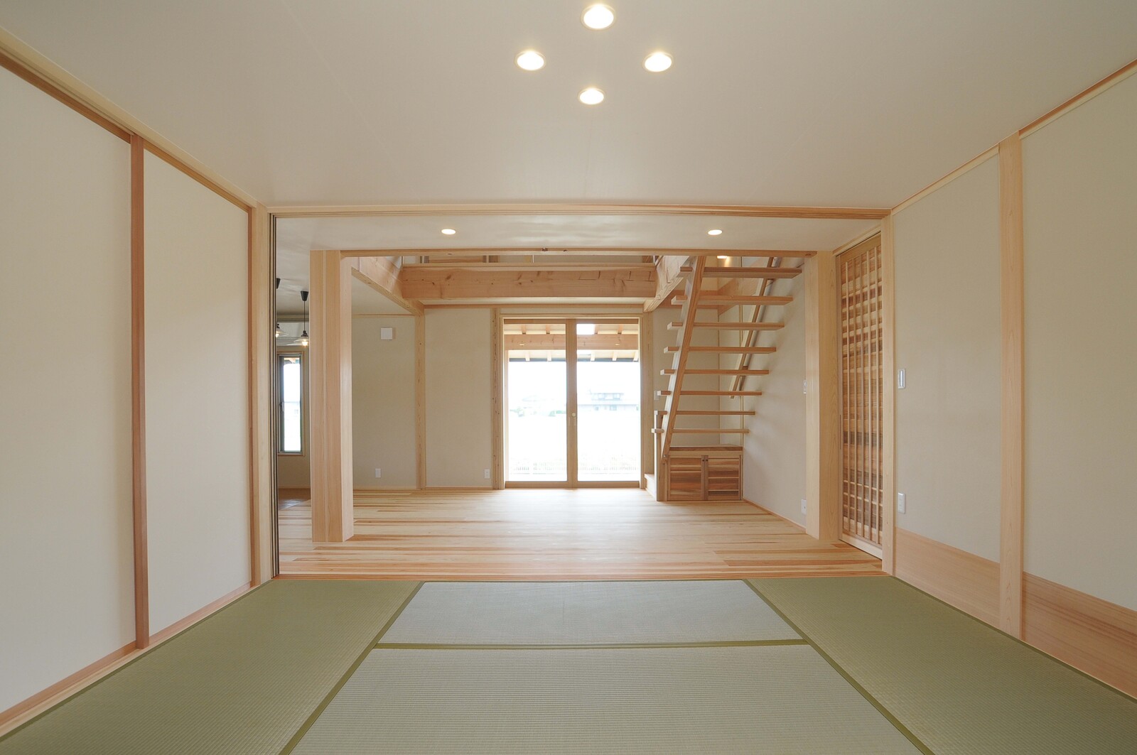 畳の和室から木の床のリビングと階段を望む
